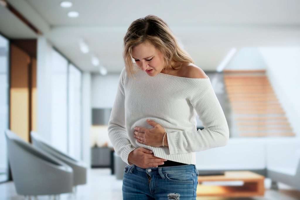 Woman holding stomach in pain 101536766 YI Woman with stomach pain representing digestive issues, IBS, bloating, and gastrointestinal disorders